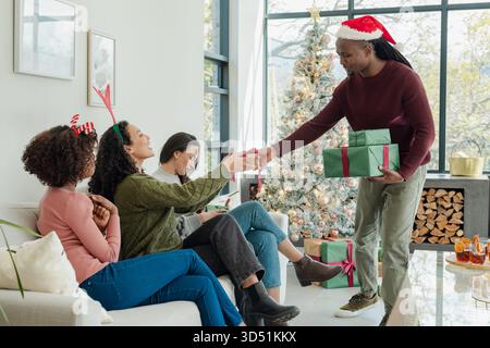 Verschiedene Freunde tauschen gewickelte Geschenke auf dem Sofa zu Hause am Weihnachtsbaum und am Kaffeetisch aus Stockfoto
