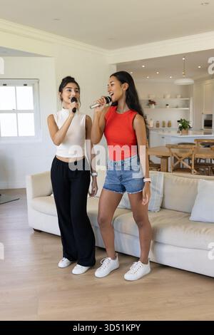 Verschiedene Freundinnen singen Karaoke im Wohnzimmer, mit Mikrofonen und Smartwatches Stockfoto Verschiedene Freundinnen singen Karaoke im Wohnzimmer, mit Mikrofonen und Smartwatches Stockfoto