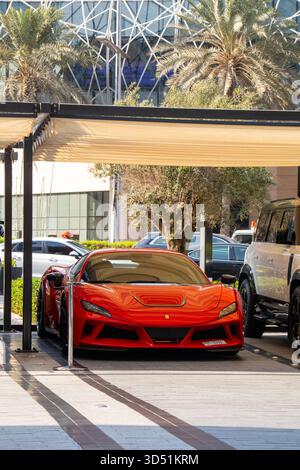 Dubai, VAE - 13. Juli 2024: Ein knallroter Ferrari F8 Tributo Supersportwagen parkt unter einem schattigen Baldachin mit Palmen und moderner Architektur Stockfoto