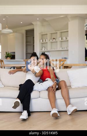 Selfie mit diversen Freundinnen, die im offenen Wohnzimmer auf der Couch sitzen, mit Smartphone Stockfoto