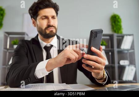 Ernsthafte Geschäftsangestellte in formeller Kleidung, die ein Mobiltelefon benutzt oder mit Partnern chatten Stockfoto