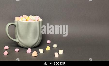 Eine graue Tasse mit einem Marshmallow-Herz auf grauem Hintergrund. Leerzeichen für Text. Stockfoto