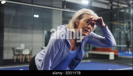 Padel, müde und reife Frau mit Schweiß für Spiel, Spiel und Training für Herausforderung. Hallenplatz, Sport und Person atmen mit Müdigkeit, Ruhe und Stockfoto