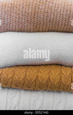 Nahaufnahme warmer Strickpullover in Pastellfarben und Beige, ordentlich gestapelt. Stockfoto