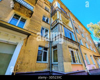 Altes gelbes Wohngebäude mit abgenutzten Balkonen und dekorativen Säulen, die Anzeichen von Putzschäden und Witterungseinflüssen zeigen. Das Foto hebt die Fassade hervor Stockfoto