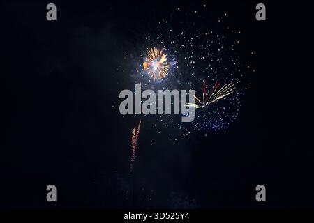 Feuerwerk explodiert gegen dunklen Nachthimmel. Mehrere bunte Bursts und Lichtstreifen beleuchten den schwarzen Hintergrund mit verschiedenen Mustern Stockfoto