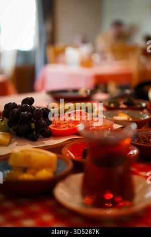 Nahaufnahme eines traditionellen türkischen Frühstückstisches mit schwarzem Tee im Glas, frischen Trauben, Tomaten, Gurken, Oliven, und verschiedene lokale Dialekte Stockfoto