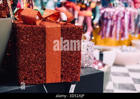 Glitzernde rote Geschenkbox mit Schleife in einer festlichen Ladenpräsentation, umgeben von anderen dekorativen Geschenken. Weihnachtsdekoration. Warschau, Polen Stockfoto