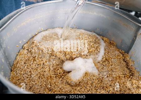 Wasser in gemahlene Gerste gießen. Gerste in einem Behälter gemahlen, Gerste mahlen. Stockfoto