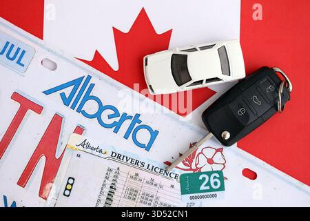 Alberta canadian Autokennzeichen und Zündschlüssel auf der Flagge von Kanada Nahaufnahme. Führerschein- und Zulassungskonzept Stockfoto