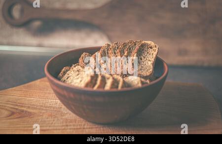 Knusprige goldene Croutons in einer rustikalen Tonschale auf einer Küchenarbeitsplatte, mit der Textur des Holzbretts dahinter für eine natürliche, heimelige Atmosphäre Stockfoto