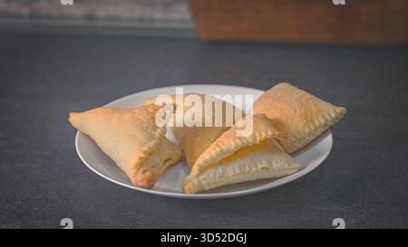 Frisch gebackenes Blätterteiggebäck liegt auf einem hölzernen Küchentisch, noch warm aus dem Ofen, und füllt das Haus mit einem gemütlichen, buttrigen Aroma. Ein rustikales Haus Stockfoto