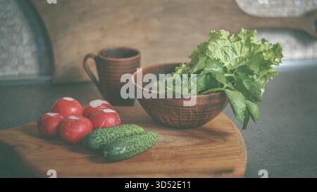 Ein Teller mit frisch geernteten Radieschen, Gurken und frischen Kräutern auf einem Holztisch in einer Küche, der an Einfachheit vom Bauernhof zum Tisch erinnert Stockfoto