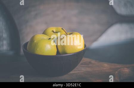 Frische Äpfel in einer rustikalen Tonschale auf einem Küchentisch angeordnet. Natürliche Texturen und warmes Licht schaffen eine gemütliche Atmosphäre Stockfoto