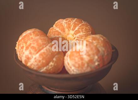 Geschälte Zitrusfrüchte in einer Tonschale auf einer Holzoberfläche angeordnet, sonnige helle Farbe betont die Frische Stockfoto