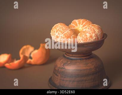 Frisch geschälte Mandarinenstücke auf einem Steingut-Teller angeordnet, lebhafte sonnige Farbe auf rustikaler Holzoberfläche Stockfoto
