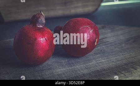 Saftige ganze Granatäpfel in einer Keramikschale auf einem hölzernen Schneidebrett, Top-down-Küchenszene mit natürlichen Texturen Stockfoto