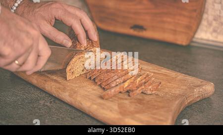 Wohnküche. Ein Mann schneidet ein Baguette mit dunklem Buchweizenbrot auf einem Holzschwein Stockfoto