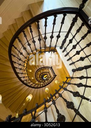 Wendeltreppe von oben mit dunklen Eisenbalustern und leuchtenden Pendelleuchten schaffen dramatische Kurven und ein warmes Ambiente Stockfoto