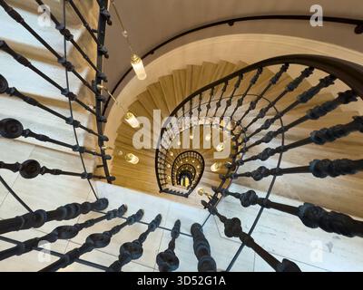 Wendeltreppe von oben mit geschwungenem Geländer warme Pendelleuchten Steintreppen schaffen Tiefe und Eleganz in der architektonischen Innenatmosphäre Stockfoto