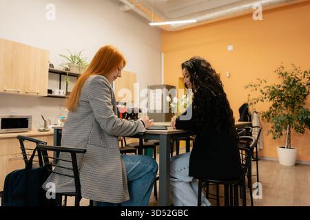 Zwei Frauen diskutieren Dokumente in einem modernen Pausenbereich und arbeiten gemeinsam an einem Projekt zusammen Stockfoto