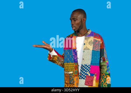Ein schwarzer Mann trägt eine bunte Patchworkjacke, mit geöffneter Hand Gesten Stockfoto