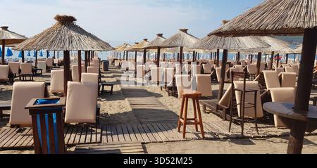 Sandstrand in Bečići, Montenegro, mit Reihen leerer Liegestühle und Strohschirme unter hellem Sommerhimmel. Perfekte Urlaubsatmosphäre am Meer. Stockfoto