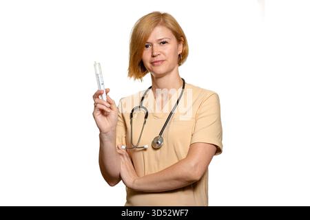 Eine Ärztin oder medizinisches Fachpersonal hält eine medizinische Spritze in einer Hand. Sie trägt eine beige Uniform und sieht ernsthaft in die Kamera. Die Stockfoto