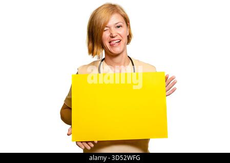 Eine Ärztin, eine Angestellte im Gesundheitswesen. Sie hält ein rechteckiges Blatt gelbes Papier in beiden Händen und lächelt spielerisch und humorvoll und schaut auf die Stockfoto