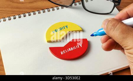 Handschrift neben Gültigkeit und Zuverlässigkeit Holzpuzzleteile auf einem Notizbuch mit Brille für Forschungs- und Qualitätskonzepte. Stockfoto