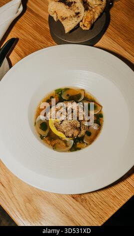 Ein weißer Teller mit einer Speise drauf. Der Teller steht auf einem Holztisch. Das Essen auf dem Teller ist eine Suppe mit Gemüse Stockfoto