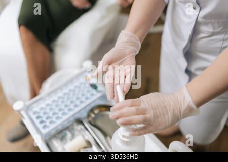 Close-up-Draufsicht des Arztes in Schutzhandschuhen, die Hände mit Pumpe Antiseptikum auf tragbarem Wagen vor dem Eingriff wie Blut desinfizieren Stockfoto