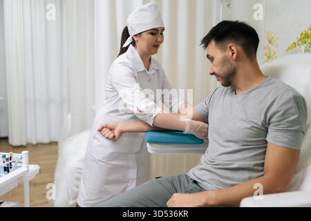 Seitenansicht eines Mediziners in Uniform und Handschuhen zur Vorbereitung der Blutentnahme von männlichen Patienten im Untersuchungsstuhl in der Moderne Stockfoto