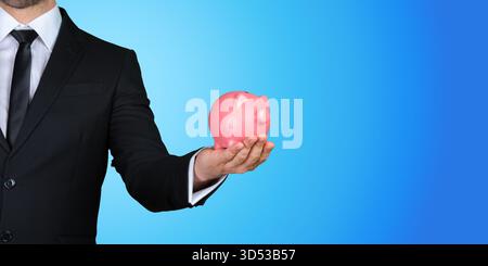 Eine pinkfarbene Schweinebank vor blauem Hintergrund halten, während sie einen schwarzen Anzug trägt Stockfoto