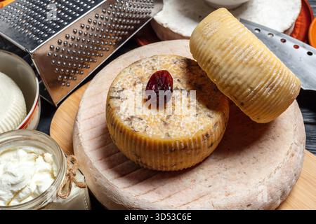 Einzigartige Käseauswahl mit Kräutern auf einem Holzbrett in einer rustikalen Küche Stockfoto