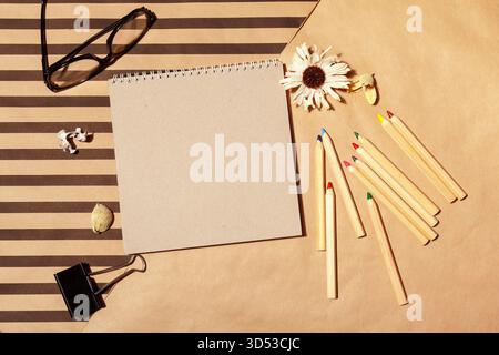 Kreativer Arbeitsbereich mit leerem Notizbuch und farbenfrohen Zeichenwerkzeugen auf gestreiftem Hintergrund Stockfoto