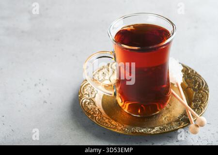 Türkischer schwarzer Tee. Eine Glasschale türkischer schwarzer Tee und knuspriger türkischer traditioneller Bagel auf grauem Betontischhintergrund. Frühstücksgebäck-Konzept. Traditionelles türkisches Heißgetränk. Stockfoto