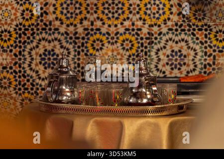 Marokkanische Pfefferminztee-Teekannen und -Gläser auf einem gefliesten Mosaikhintergrund. Elegantes Ambiente in einem traditionellen marokkanischen Restaurant. Stockfoto
