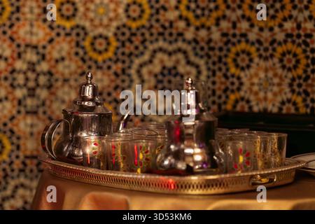 Marokkanische Pfefferminztee-Teekannen und -Gläser auf einem gefliesten Mosaikhintergrund. Elegantes Ambiente in einem traditionellen marokkanischen Restaurant. Stockfoto