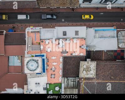 Aus der Vogelperspektive auf eine Dachterrasse mit Fliesenboden, Tischen, Stühlen und einem Pool, im Kontrast zur umliegenden Stadtlandschaft Quito, Ecuador. Stockfoto