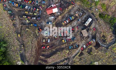 Aus der Vogelperspektive eines Fahrzeugfriedhofs mit einer Mischung aus bunten Autos und Lastwagen, die in der dunklen Erde in der Nähe des Mount Batur, Bali, Indonesien, verstreut sind. Stockfoto