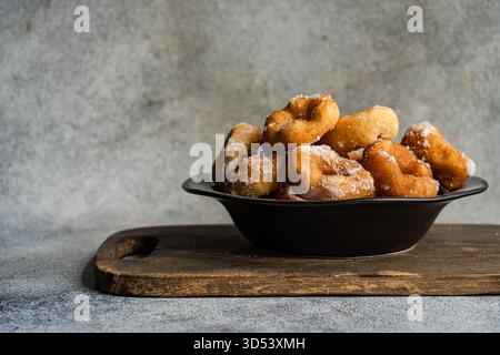 Nahaufnahme einer Schüssel mit selbstgemachten Donuts, die mit Puderzucker auf einem hölzernen Schneidebrett bestäubt sind Stockfoto