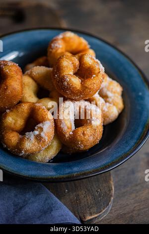 Aus nächster Nähe auf eine Schüssel mit selbstgemachten Donuts, die mit Puderzucker auf einem hölzernen Schneidebrett bestäubt sind Stockfoto