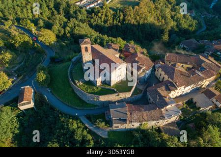 Blick aus der Vogelperspektive auf die alte Steinkirche und Festung auf einem Hügel, in goldenem Sonnenlicht getaucht, umgeben von üppigen grünen Wäldern, Trassilico, Toskana Stockfoto