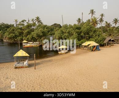Blick aus der Vogelperspektive auf einen ruhigen Fluss, der auf üppige grüne Vegetation mit Gebäuden inmitten von Bäumen trifft, Lagos, Nigeria. Stockfoto