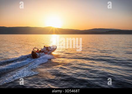 Blick aus der Vogelperspektive auf ein SPORTRIPPBOOT, das während des Sonnenuntergangs im Sommer mit Geschwindigkeit über das ruhige Meer fährt Stockfoto