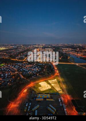 Nächtlicher Blick auf den beleuchteten Skatepark und Zirkuszelt mit kontrastfarbenem Wohnwagen und dichtem urbanem Raster, die lebendige Beleuchtung offenbart Schicht Stockfoto