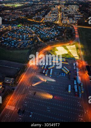 Nächtlicher Blick auf den Circus Renz, ein heller Skatepark und gestreifte Zelte leuchten neben organisiertem Busparkplatz, Wohnraster und warmer Straße Stockfoto