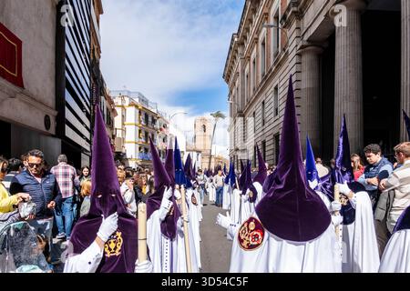 Ostersemana Santa Prozession in Sevilla, Spanien, 15. April 2025. Nazarenos in weißen Gewändern und violetten Kapuzen spazieren durch historische Straßen, umgeben von ihnen Stockfoto