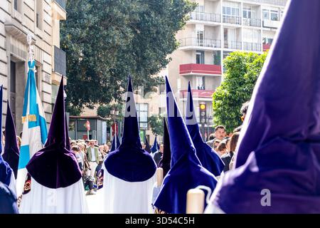 Ostersemana Santa Prozession in Sevilla, Spanien, 15. April 2025. Nazarenos in weißen Gewändern und violetten Kapuzen spazieren durch historische Straßen, umgeben von ihnen Stockfoto